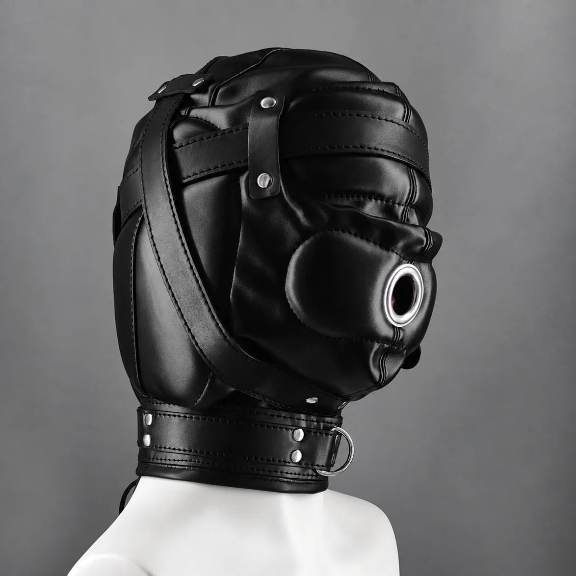 Side profile of a black leather bondage hood with padded eye covering, reinforced leather straps, a metal mouth ring, and an adjustable neck collar.