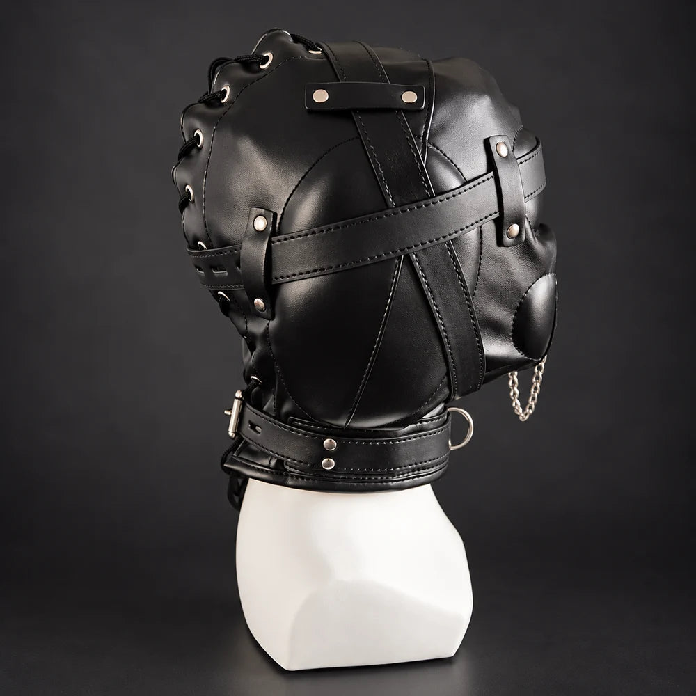 Side profile of a black leather bondage hood featuring adjustable leather straps, stitched panels, silver rivets, studded mouth cover, hanging metal chain and matching neck collar.