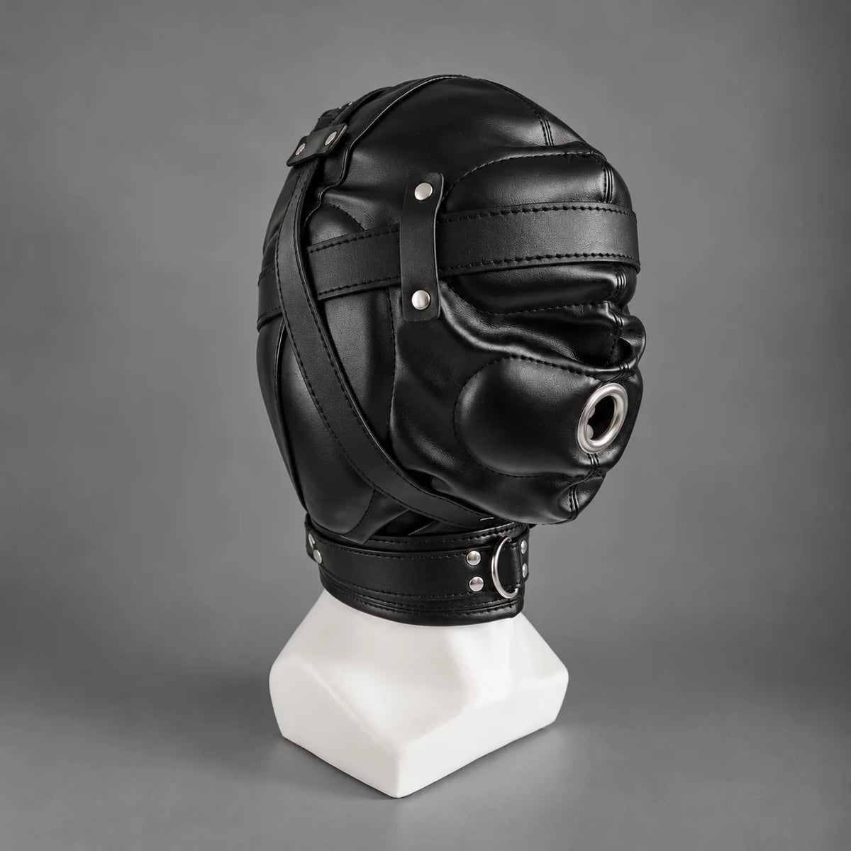 Black leather bondage hood displayed on a mannequin, showing its side profile, metal mouth ring, stitched leather panels, and adjustable neck collar.