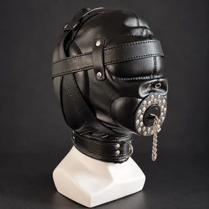 Black leather bondage hood with padded eye covering, adjustable head straps, studded mouth cover, silver chain and leather neck collar, displayed on a white mannequin in three-quarter side view.