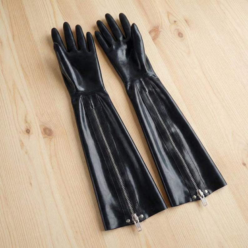 Black latex gloves with zippers laid flat on a light wood surface, highlighting the material texture.
