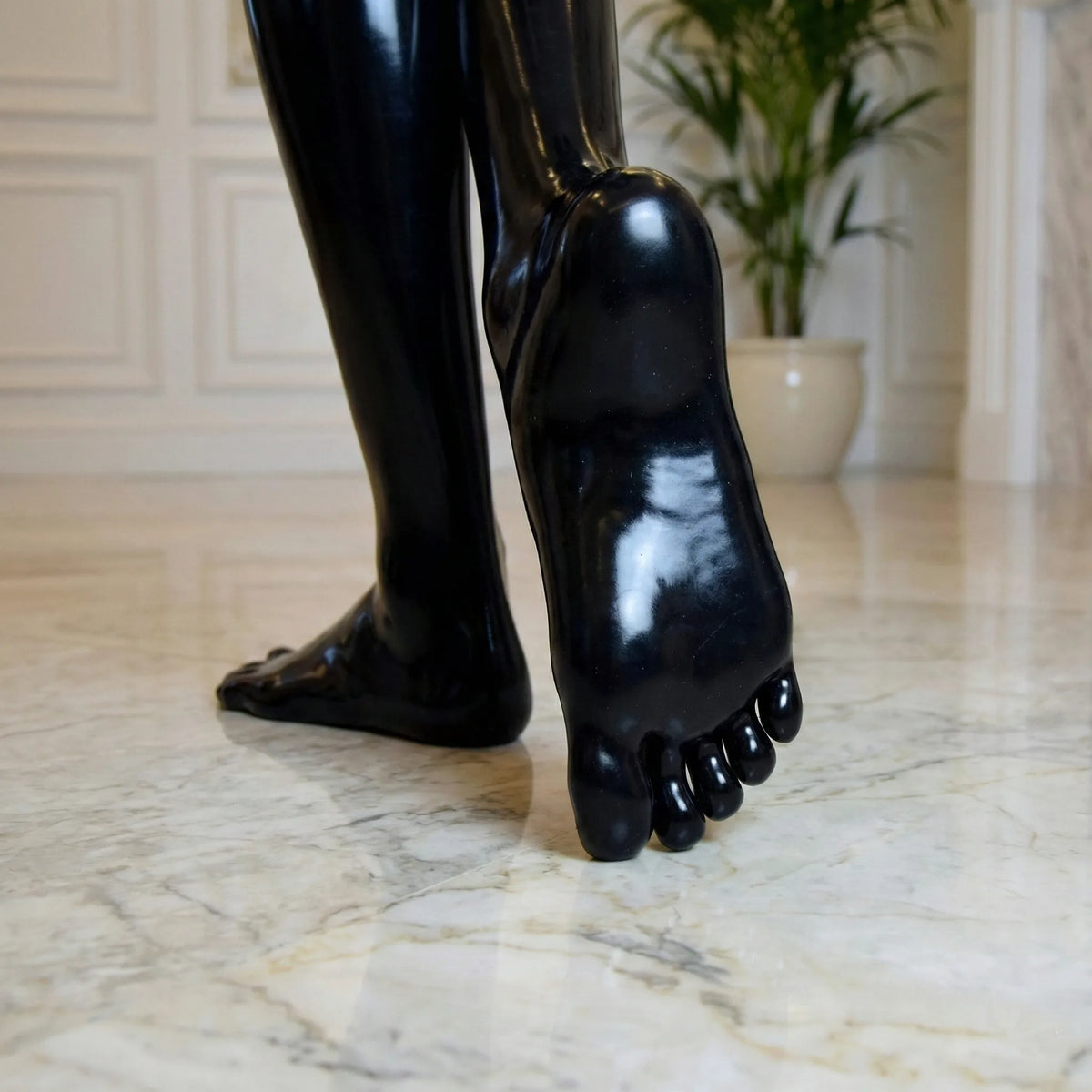 Sole and five toes of a glossy black latex toe sock on a marble floor