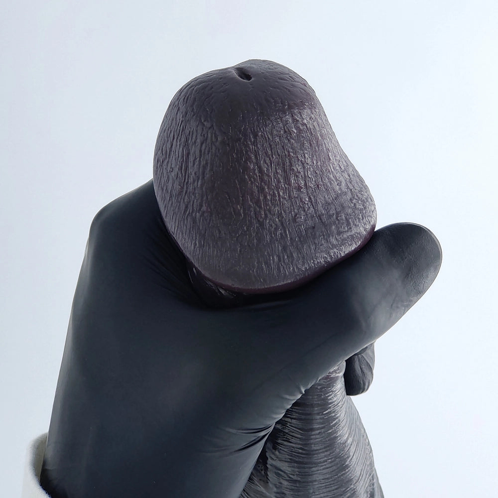 Close-up of the glans area of a demonstration model fitted with the Mega Veins penis sleeve, clearly showing its detailed and realistic texture, held with a black glove