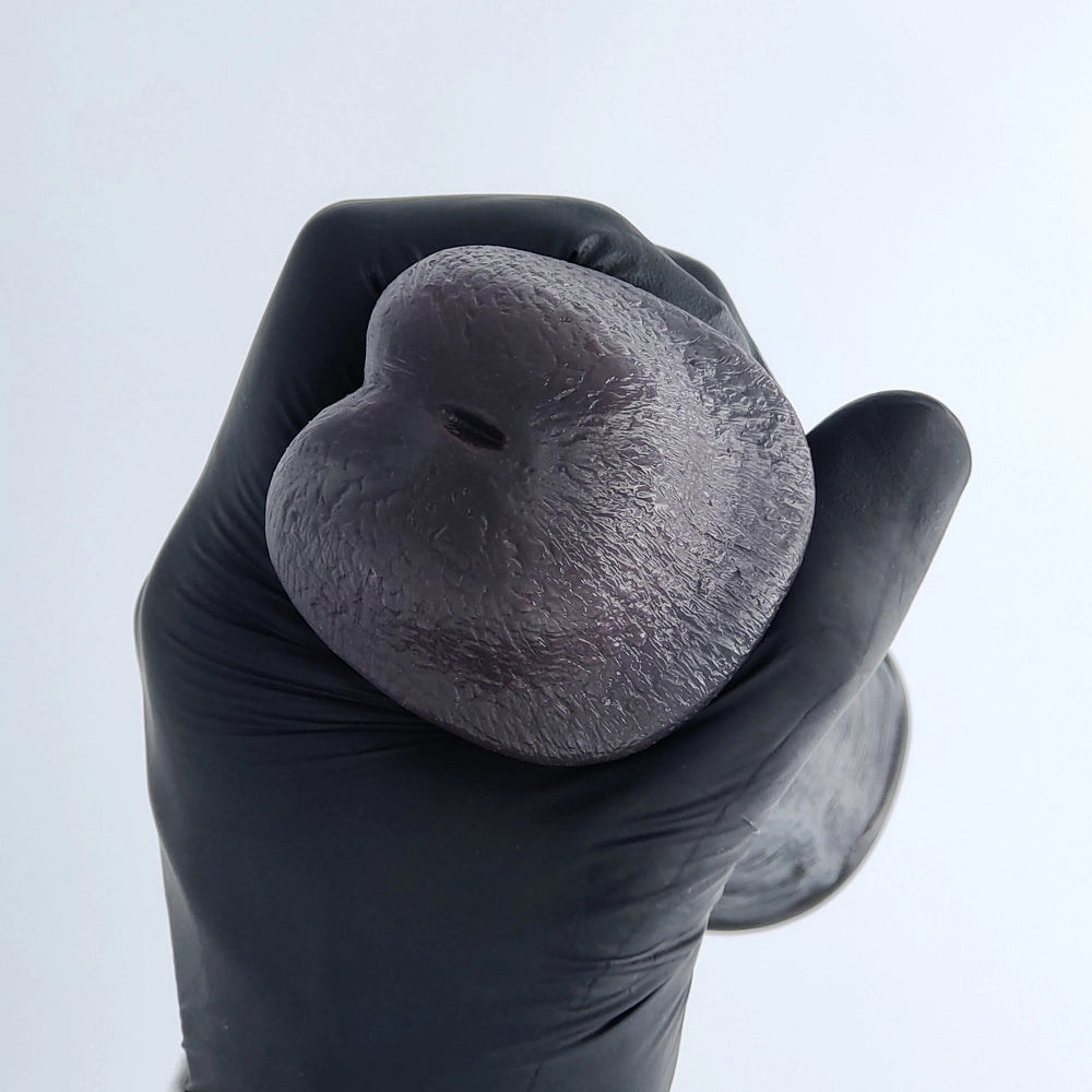 Close-up of the tip of a demonstration model showing the Mega Veins penis sleeve with a decorative, closed urethral opening (non-functional), held with a black glove – adult toy