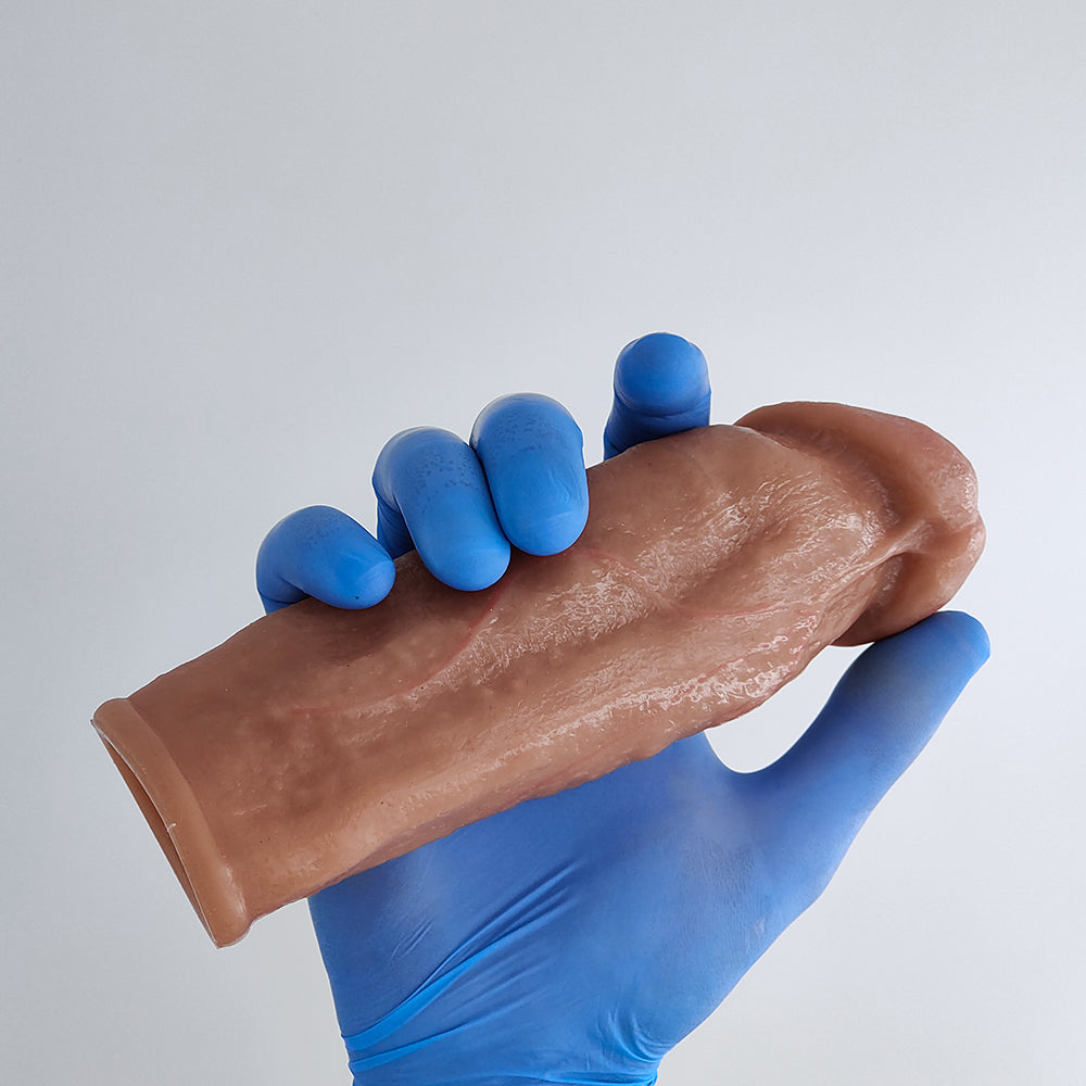 a blue gloved hand supports the realistic penile sleeve shown in the back, detail of the frenulum and skin