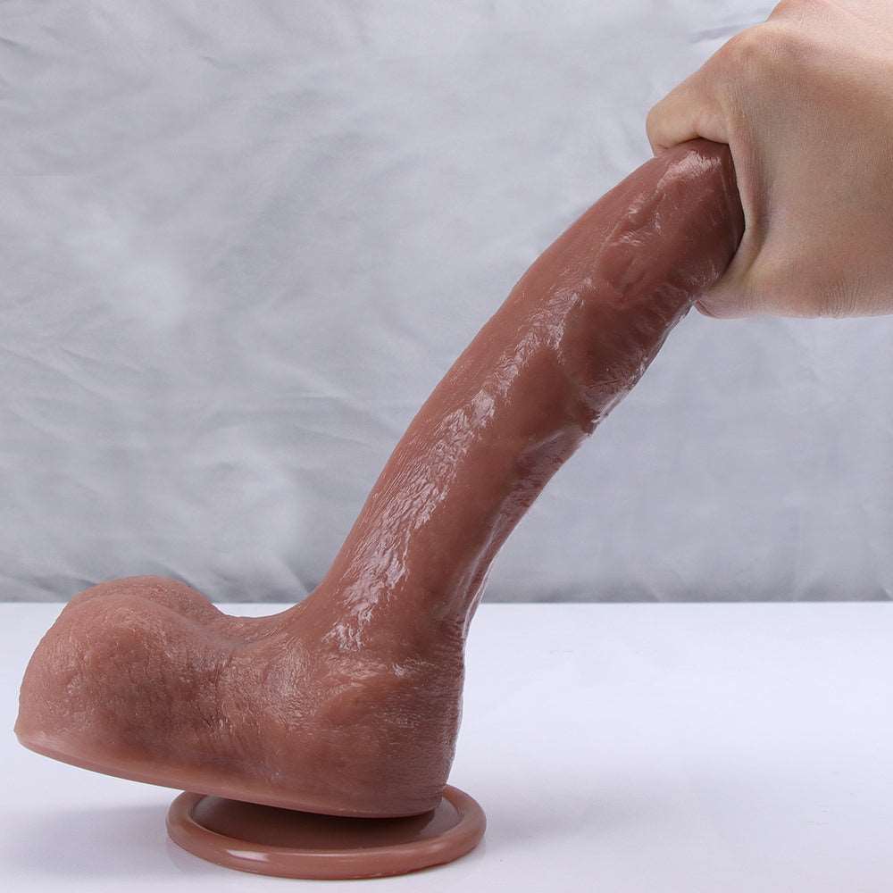 Sculpture Brown dual-density dildo standing on its suction cup base, held by hand to show the veined shaft