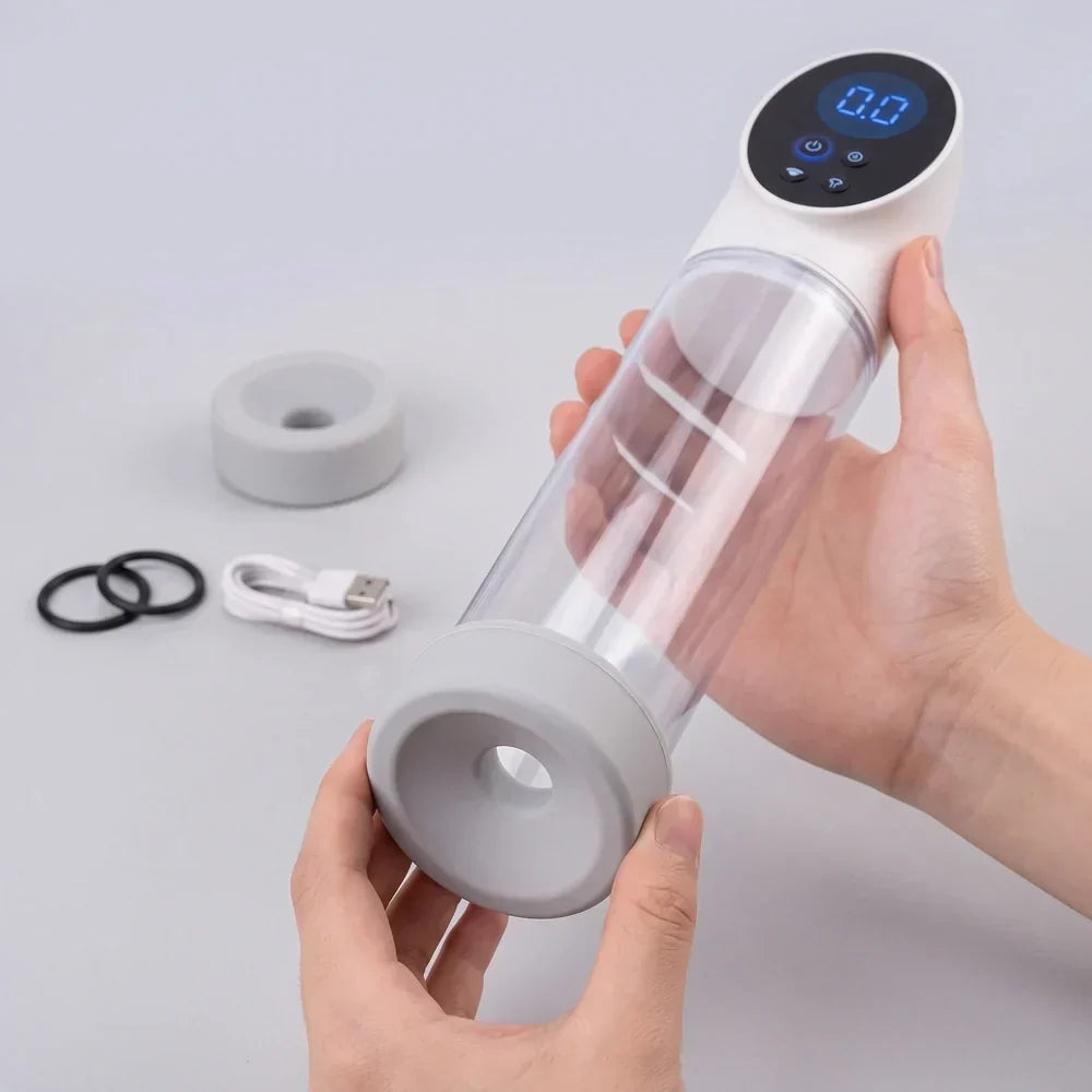 A digital penis pump set, featuring the clear cylinder unit with a blue LED control display (showing '0.0'), two gray silicone sleeves, two black constriction rings, and a white USB charging cable, presented on a gray surface.