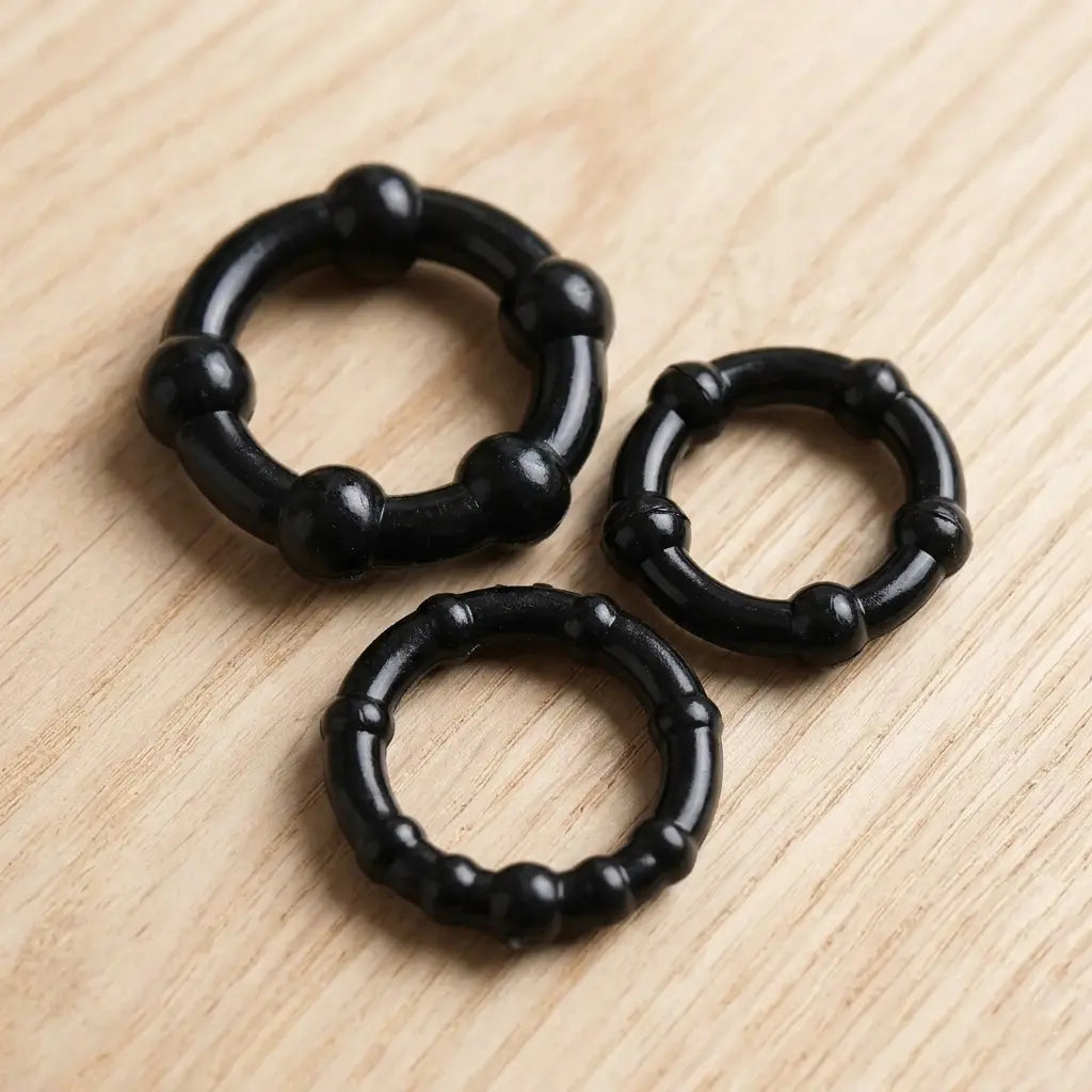three black silicone cock rings of different sizes on a light-colored wooden surface