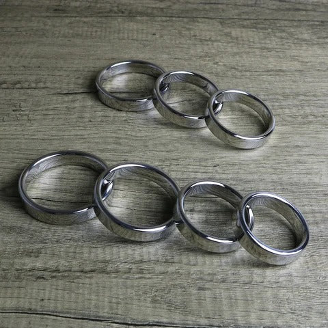 seven steel cock rings of various sizes on a wooden table