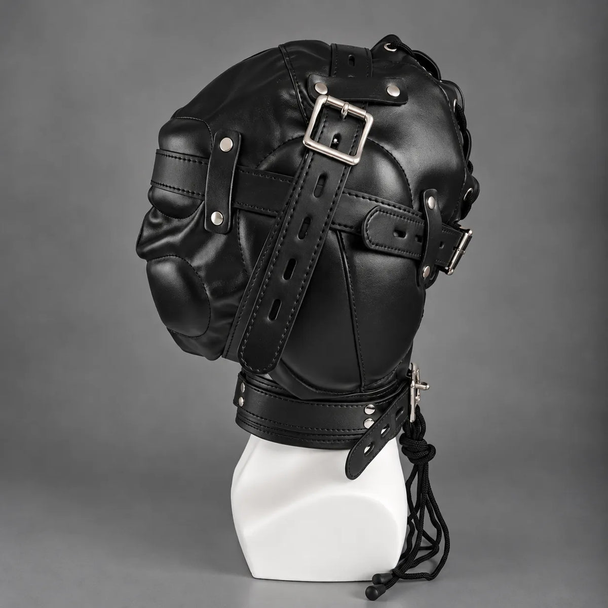 Opposite side view of a black leather bondage hood featuring multiple adjustable buckle straps, padded leather panels, metal hardware, and hanging laces.