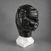Black leather bondage hood displayed on a mannequin, showing its side profile, metal mouth ring, stitched leather panels, and adjustable neck collar.