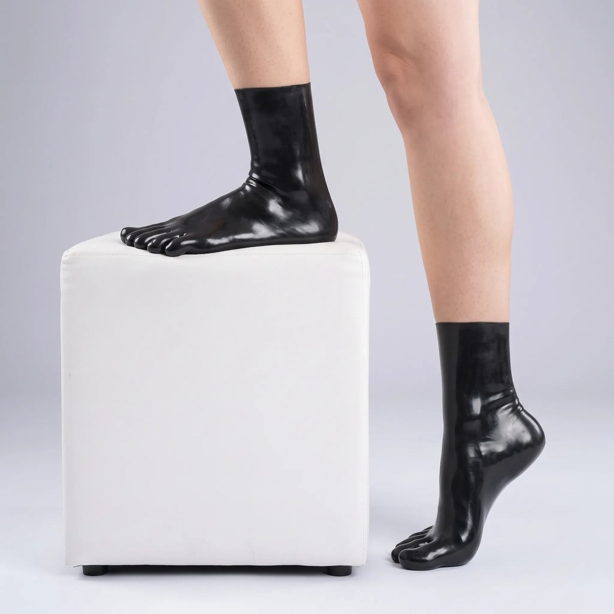 Black short latex toe socks worn with one foot resting on a white pouf, glossy finish