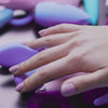 A hand caresses and displays various types of sex toys