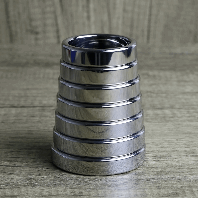 Stack of polished stainless steel cock rings in graduated sizes on a wooden surface
