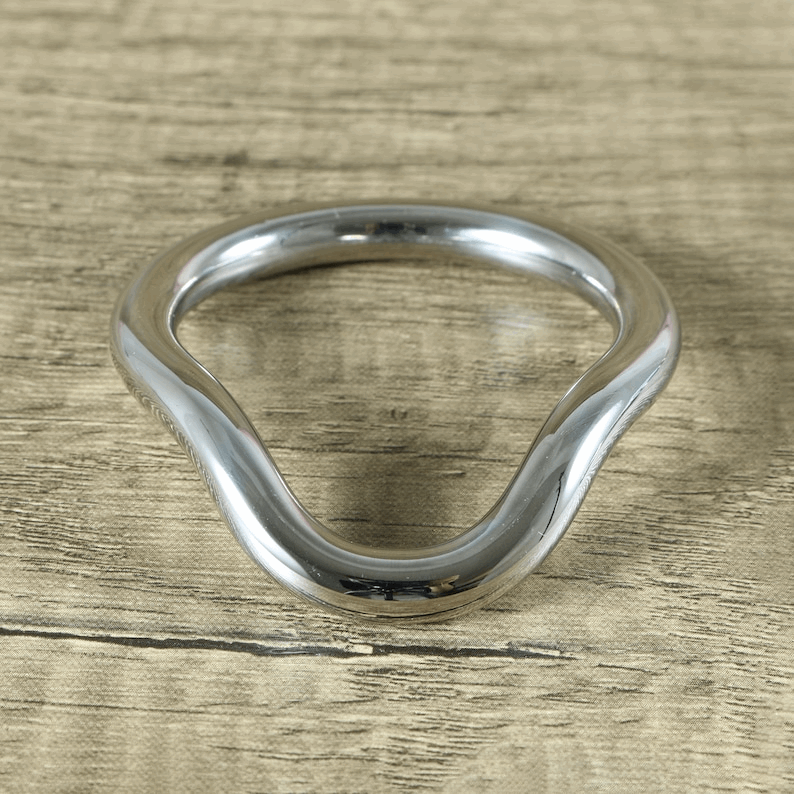 Polished stainless steel curved cock ring on a wooden surface